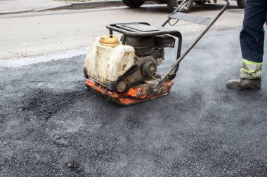 İşçi yolda asfaltı mekanik bir çarpıcı ile yokuşa sürüyor. Yol yüzeyini döşemek. Sıcak asfalt Rammer 'ın baskısı altında