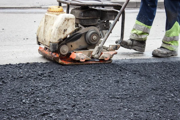 worker ramps the asphalt on the road with a mechanical rammer. laying the road surface. hot asphalt under the pressure of the rammer