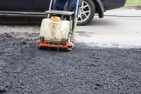 worker ramps the asphalt on the road with a mechanical rammer. laying the road surface. hot asphalt under the pressure of the rammer