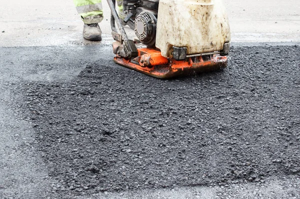worker ramps the asphalt on the road with a mechanical rammer. laying the road surface. hot asphalt under the pressure of the rammer