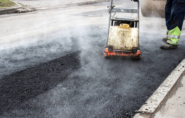 worker ramps the asphalt on the road with a mechanical rammer. laying the road surface. hot asphalt under the pressure of the rammer