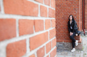 mladá krásná brunetka dívka v černé bundě a džíny stojí v blízkosti zdi gotického kostela v letní den