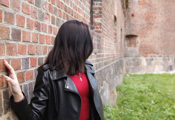 黒いジャケットの若い美少女とジーンズは晴れた日に古い要塞の壁の近くに立っています 戸外で — ストック写真