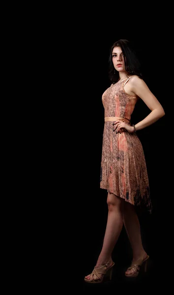 若いです美しいですブルネット女の子でベージュのドレス姿でスタジオに立って黒の背景 — ストック写真
