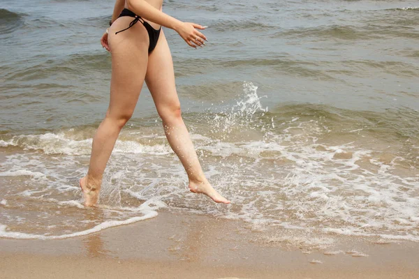 夏の晴れた日に海岸の砂の上を走る黒い水着姿の若い美少女 足を閉じて — ストック写真