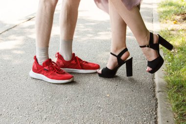 Bir erkek ve bir kadının bacakları birbirine bakıyor. Yaz günü kaldırımda dikilirken