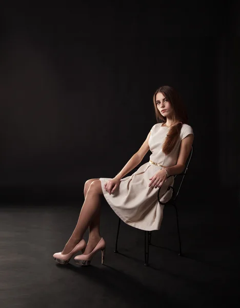 Mooi meisje in een lichte jurk zitten op de stoel — Stockfoto