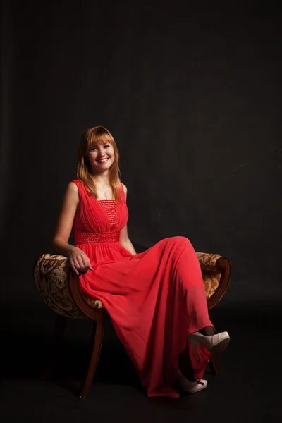 Jovem mulher bonita em vestido vermelho sentado em uma cadeira — Fotografia de Stock