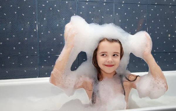 Küçük kız bir banyo oturan ve sabun köpük başında uygular — Stok fotoğraf