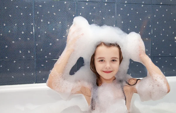 Little girl sitting in a bath with soap suds on her head — Stock Photo, Image