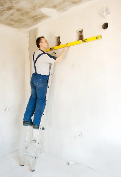 Trabajador hombre comprueba la pared con un nivel — Foto de Stock