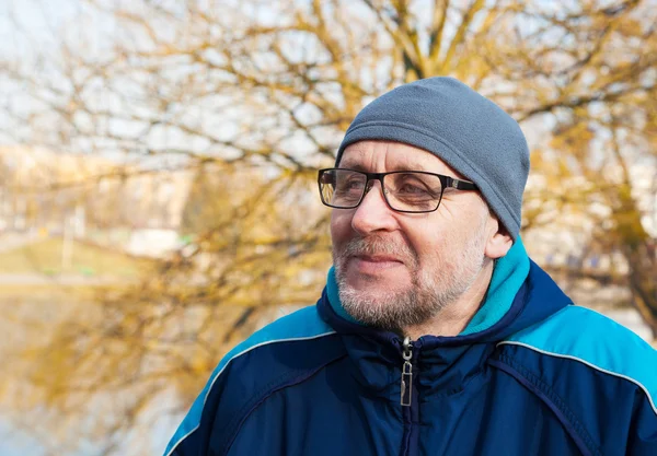 Anziano uomo con gli occhiali, un cappello grigio e giacca blu in una cit — Foto Stock