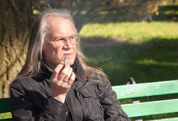 Âgé homme aux cheveux gris dans des lunettes fumant une cigarette — Photo