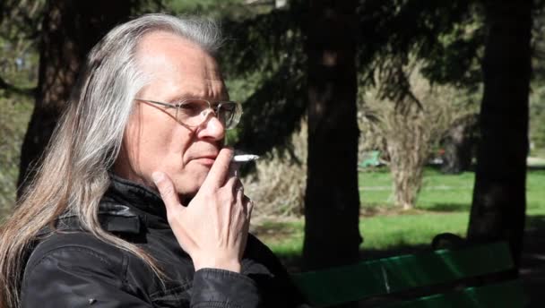 Anciano hombre de pelo gris en gafas fumando un cigarrillo — Vídeos de Stock