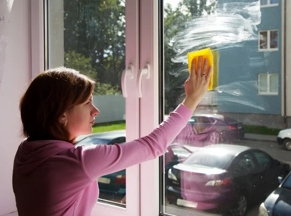 Mujer joven lavando un cristal de ventana con trapo amarillo — Foto de Stock