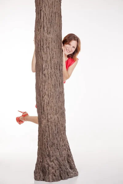 Young woman looks out from behind a tree — Stock Photo, Image