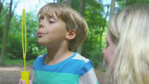 Мальчик, играющий с матерью, пускающей пузыри — стоковое видео