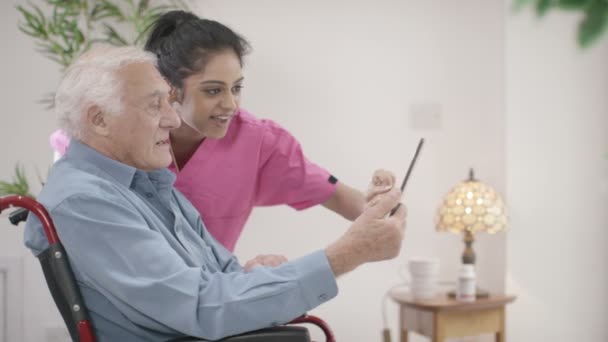 Медсестра помогает джентльмену использовать планшет — стоковое видео