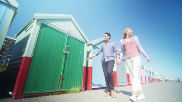 Couple passer devant des cabanes de plage colorées — Video