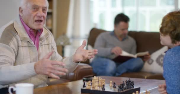 Father watches son playing chess with grandfather — Stock Video