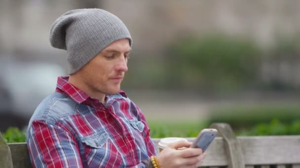 Sentado en el banco del parque con el teléfono móvil — Vídeos de Stock