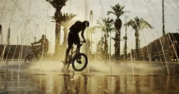 Мальчики на велосипедах охлаждаются в фонтане — стоковое видео