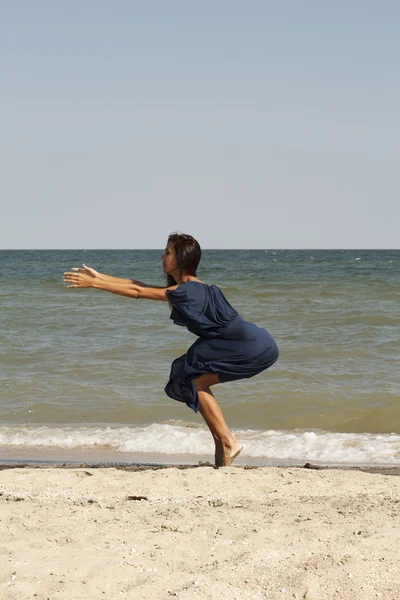 Young beautiful woman doing yoga on beach in dress — Stock Photo, Image