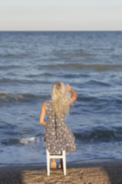 Imagem borrada da jovem mulher sentada à beira-mar na cadeira — Fotografia de Stock