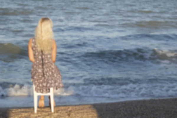 Blurred picture of young  woman sitting on seaside in chair — Stock Photo, Image