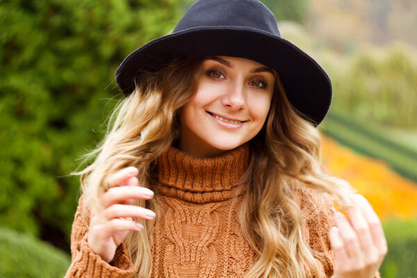 Young happy beautiful woman with curly hair wearing black hat and sweather having good time in autumn park