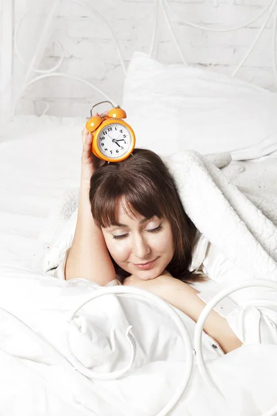 Mladá krásná žena v posteli s hodinami — Stock fotografie