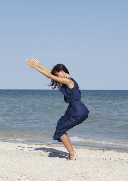 Молодая красивая женщина, занимающаяся йогой на берегу моря в синем платье — стоковое фото