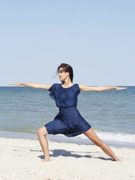 Young beautiful woman doing yoga at seaside in blue dress — Stock Photo, Image