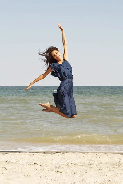 Young beautiful woman jumping at seaside in blue dress — Stock Photo, Image