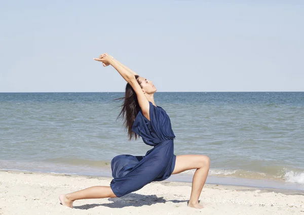 Young beautiful woman doing yoga at seaside in blue dress — Stock Photo, Image