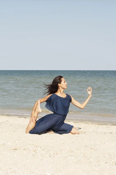 Young beautiful woman doing yoga at seaside in blue dress — Stock Photo, Image