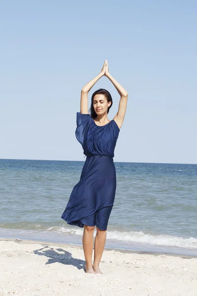 Jonge mooie vrouw doen yoga op zee in blauwe jurk — Stockfoto