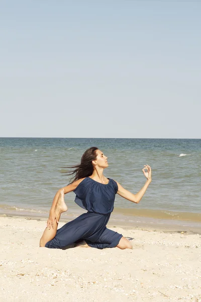 Mladá krásná žena, která dělá jóga u moře v modrých šatech — Stock fotografie