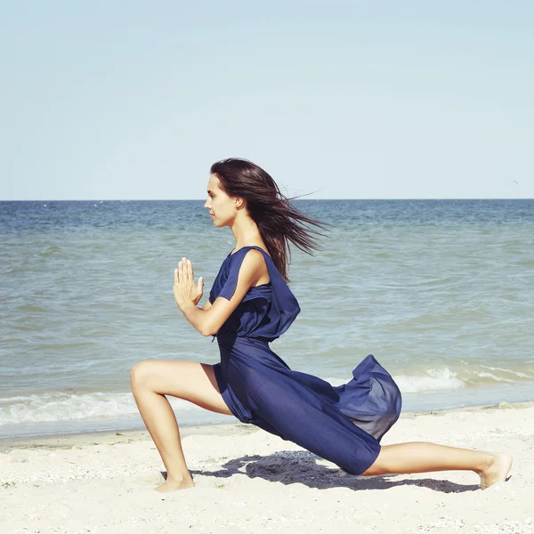Jonge mooie vrouw doen yoga op zee in blauwe jurk — Stockfoto