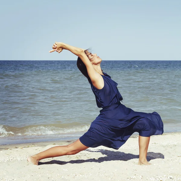 Joven hermosa mujer haciendo yoga en la playa en vestido azul —  Fotos de Stock