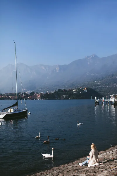 girl sitting on the shore of a mountain lake Como with yachts and birds