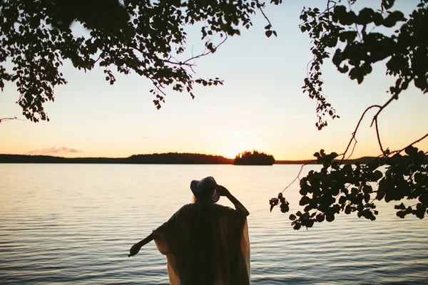 girl standing back to the view of the sunset on the lake