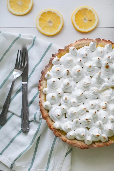 lemon tart with meringue on a table with a napkin and appliances