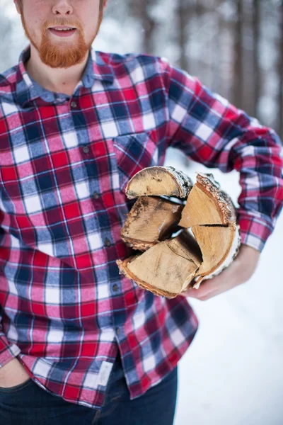 A man carries a pile of firewood in the winter forest