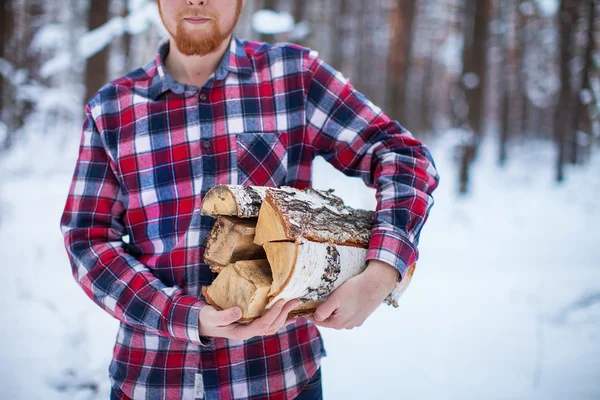 A man carries a pile of firewood in the winter forest