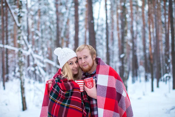 young couple sheltered plaid holding a hot tea in winter wood
