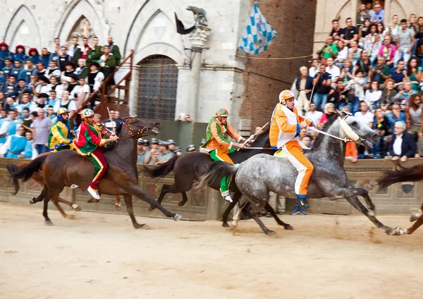 Zawodnicy rywalizują w wyścigu koni "Palio di Siena" w średniowiecznym placu "Piazza del Campo" — Zdjęcie stockowe