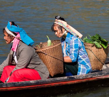 Two long-necked woman with vegetables in baskets sitting in boat, province of Mae Hong Son, Thailand