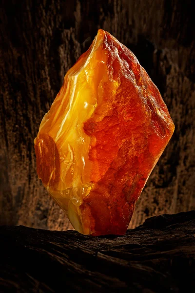 Beauty of natural raw amber. A piece of yellow opaque natural amber on large piece of dark stoned wood. — Stock Photo, Image