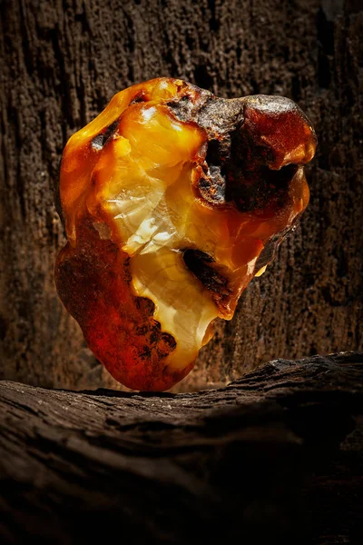 Beauty of natural raw amber. A piece of yellow opaque natural amber on large piece of dark stoned wood.